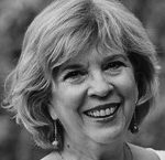 Retrato en blanco y negro de una mujer mayor, con cabello corto y ondulado, sonriendo. Lleva pendientes colgando y una expresión amable.